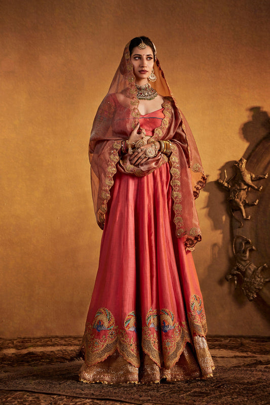 Model in a vibrant sorbet peach silk lehenga, ornate design, flowing fabric, traditional South Asian wedding dress.