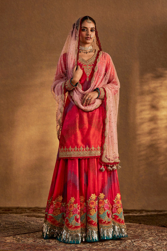 Model in a vibrant peach amber kurta set with intricate embroidery, flowing silhouette, cultural fashion, festive attire.