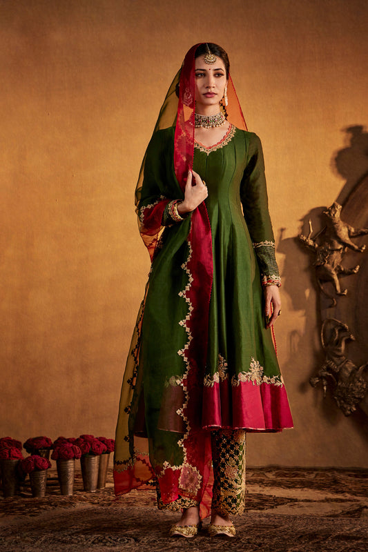 Woman in dark green Abha kurta set with red and gold accents, traditional South Asian attire.