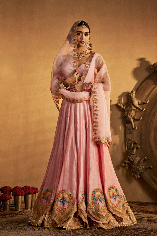Model in a soft pink silk lehenga, intricate gold embroidery, elegant bridal attire, South Asian formal fashion.