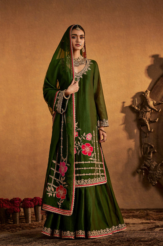 Model in a deep green floral sharara set, vibrant embroidery, traditional South Asian formal attire, festive occasion wear.