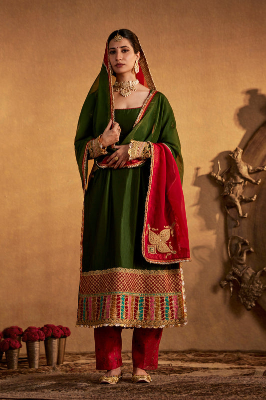 Woman in dark green Abha kurta set with red and gold accents, traditional South Asian attire.