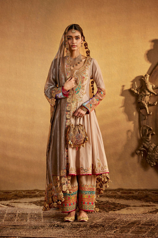 Woman in an embroidered beige traditional South Asian dress, long sleeves, wide skirt, intricate details, formal ethnic wear.