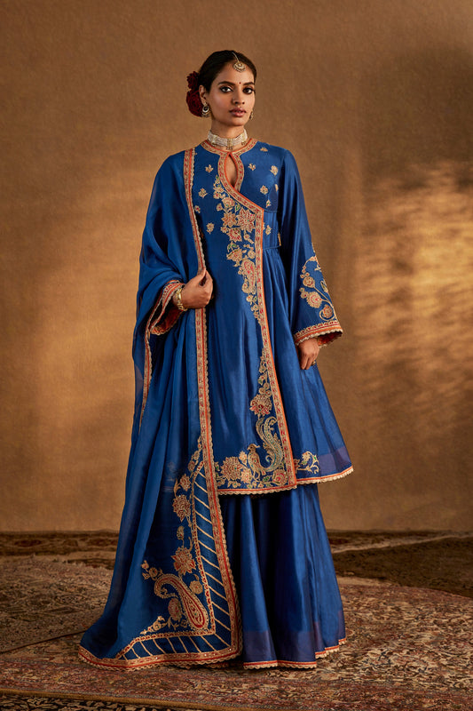 Model in an elegant lapis blue silk sharara set with intricate gold embroidery, traditional South Asian formal wear, flowing.