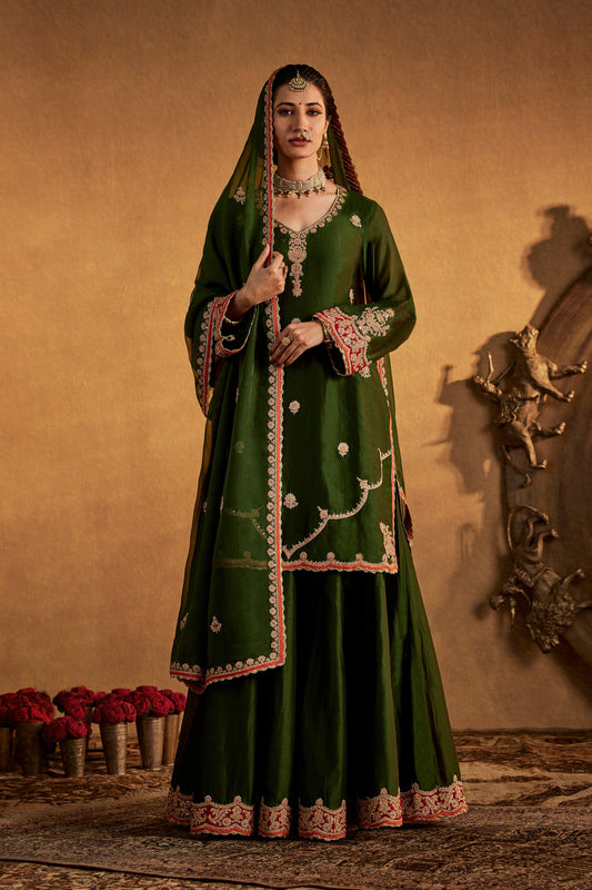 Model in a pine green sharara set with intricate embroidery, traditional South Asian formal wear, flowing skirt, elegant.