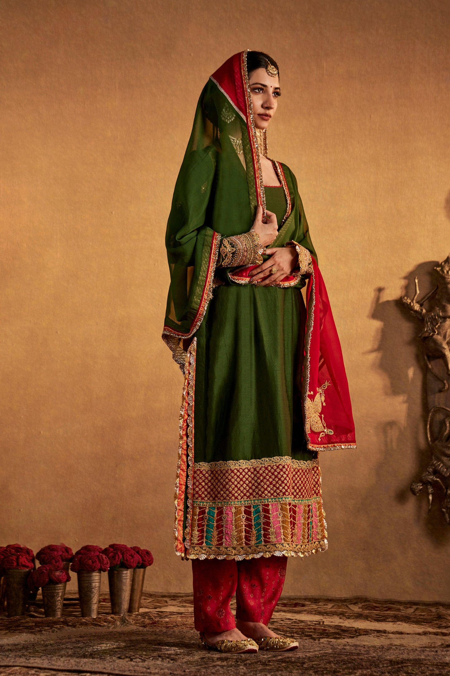 Woman in dark green Abha kurta set with red and gold accents, traditional South Asian attire.