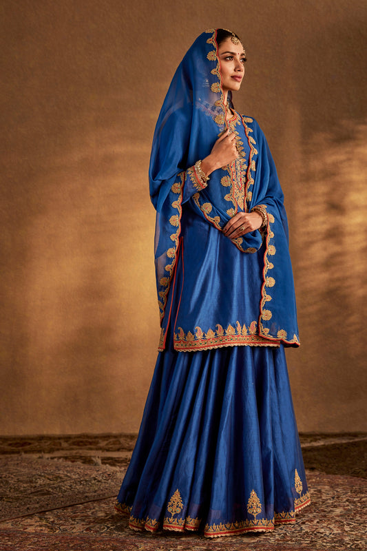 Model in a lapis blue silk sharara set, gold embroidery, traditional South Asian formal wear, flowing skirt, elegant.