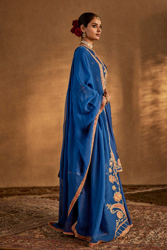 Model in an elegant lapis blue silk sharara set with intricate gold embroidery, traditional South Asian formal wear, flowing.