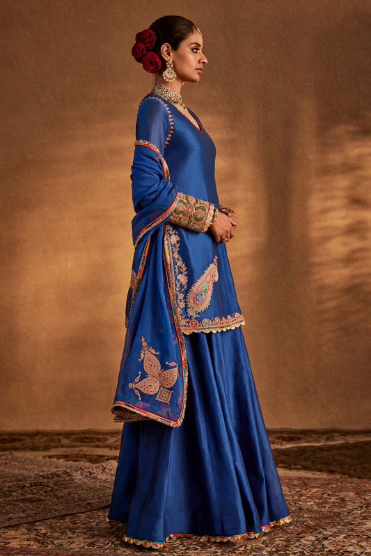Model in a deep blue sharara set with peacock embroidery, flowing skirt, traditional South Asian formal dress, stunning.