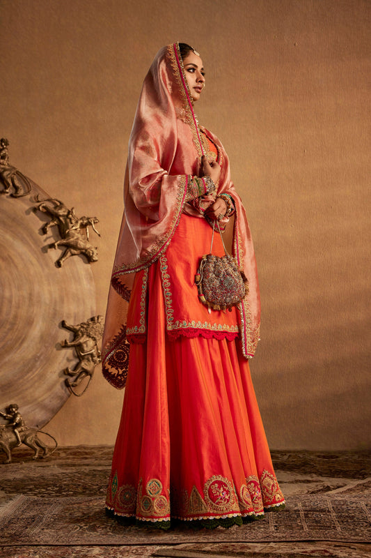 Model in a peach amber sharara set, burnt orange skirt, flowing silhouette, intricate details, cultural attire, festive.